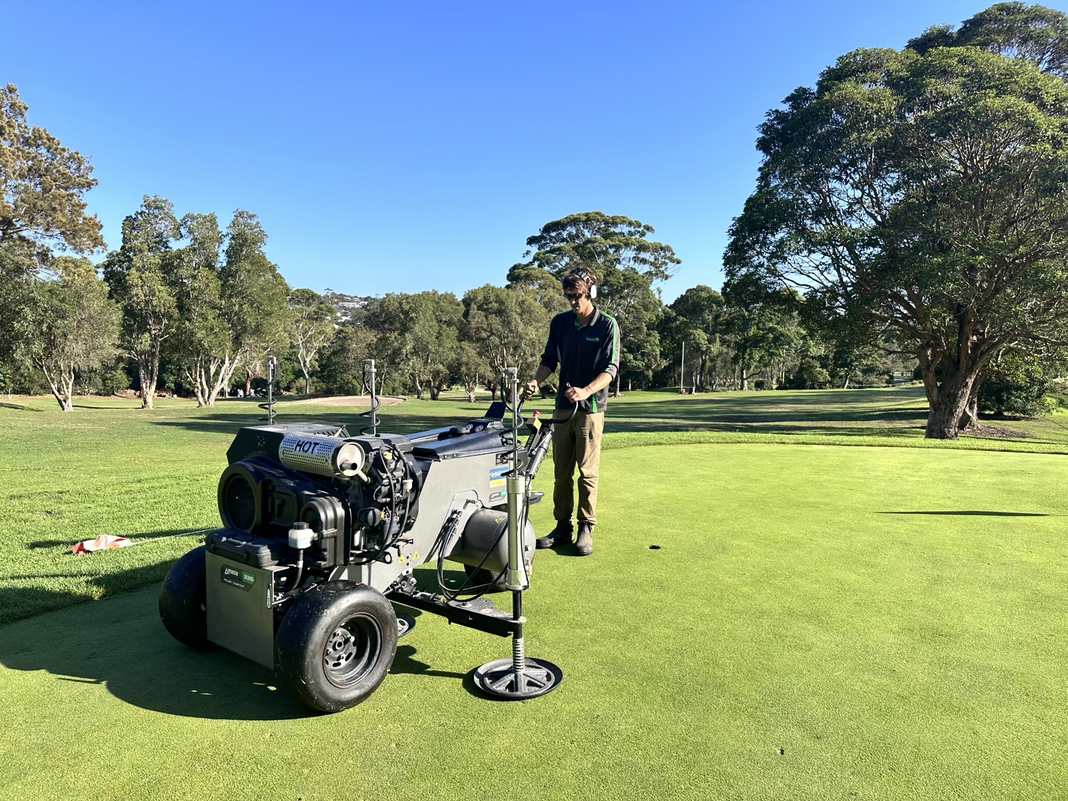 A technician operating an aeration machine on a golf green